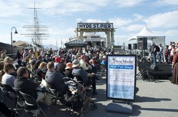 A crowd of people on Hyde Street Pier sitting on chairs and listening to music performers.